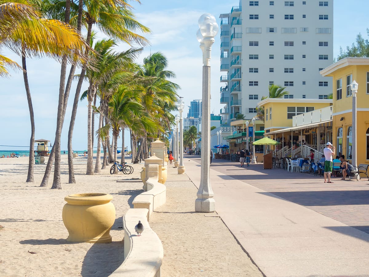 The Broadwalk on Hollywood Beach, people walking past the cafes, the sand and the water to the left
